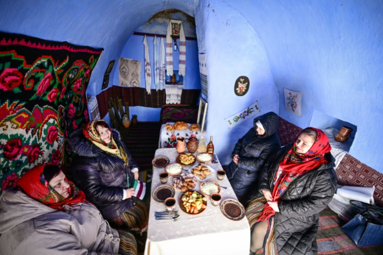 Des femmes du village de Rogojeni, en costumes traditionnels, prennent un repas à l'intérieur d'une maison-musée "basca", le 4 janvier 2026 en Moldavie ( AFP / Daniel MIHAILESCU )