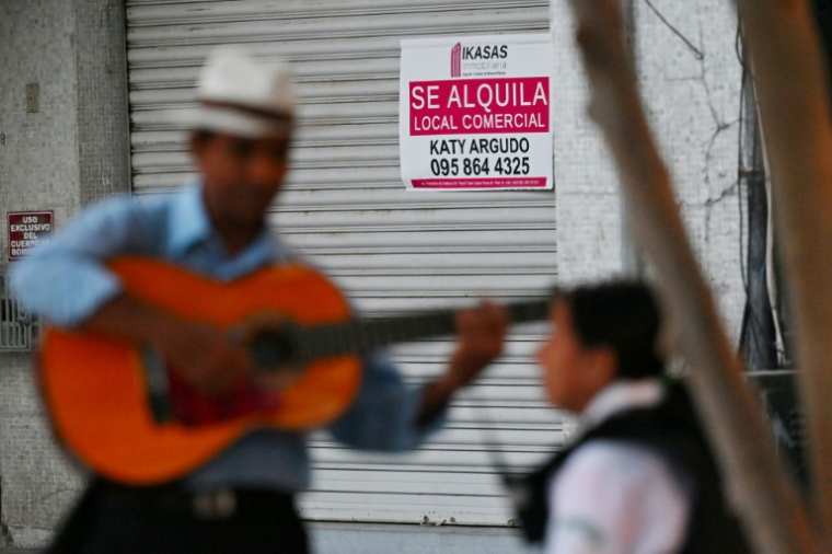 Un chanteur de rue joue de la guitare devant un local commercial à louer à Guayaquil, en Équateur, le 9 août 2025 ( AFP / MARCOS PIN )