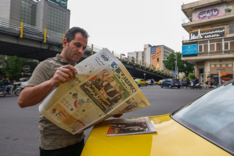 Un Iranien lit un journal dans une rue de Téhéran, le 12 avril 2025, avec en première page les pourparlers irano-américains sur le nucléaire ( AFP / ATTA KENARE )