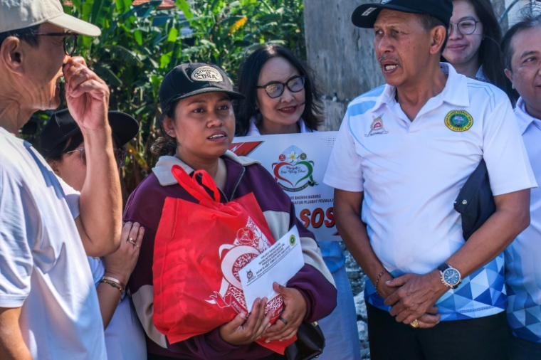 Ruth Deidree Boelan (c), dont les proches ont disparu lors des récentes inondations, reçoit la visite de membres de sa famille sur le site de son ancienne résidence à Mengwi, sur l'île touristique de Bali, le 2 octobre 2025 en Indonésie ( AFP / BAY ISMOYO )