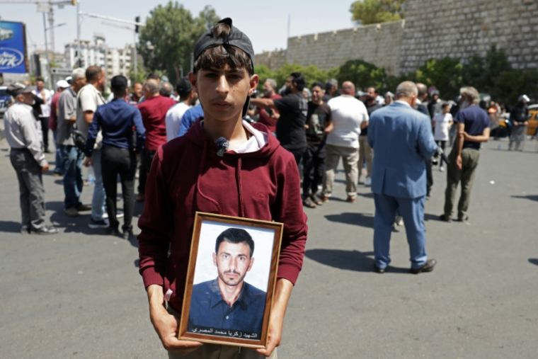 Un jeune Syrien porte la photo d'un proche, à proximité du tribunal de Damas où a été condamné à mort en son absence le président déchu Bachar al-Assad le 11 août 2026 ( AFP / Bakr ALkasem )