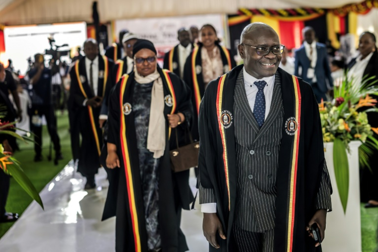 Le président de la Commission électorale ougandaise, le juge Simon Mugenyi Byabakama (D), marche avec d’autres commissaires de haut rang après l’annonce des résultats partiels de l’élection présidentielle ougandaise, à  Kampala le 16 janvier 2026 ( AFP / Luis TATO )