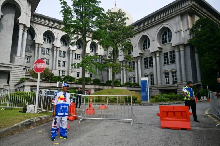 Un partisan de l'ex-Premier ministre malaisien Najib Razak (à gauche), habillé aux couleurs de son parti, se tient devant le palais de justice de Putrajaya, en Malaisie, le 26 décembre 2025 ( AFP / Mohd RASFAN )