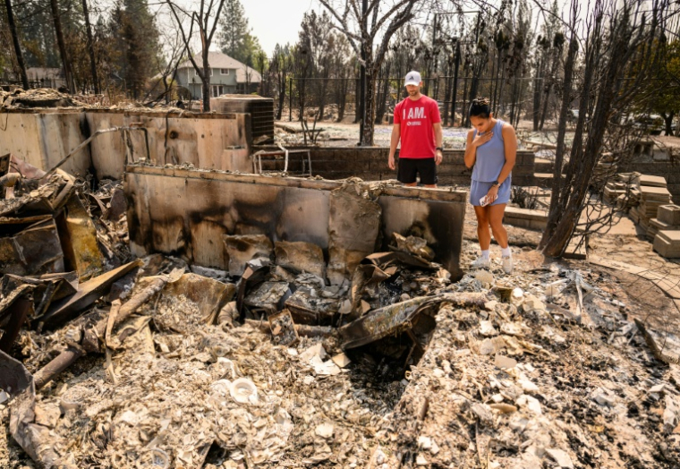 Une femme et son mari tentent de voir si certaines de leurs affaires ont résisté aux flammes, dans les ruines de leur maison réduite en cendres, à Spokane, dans l'Etat de Washington, le 4 août 2026 ( AFP / Josh Edelson )