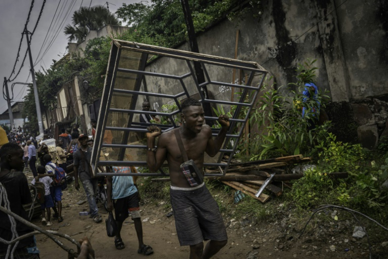 Un homme porte une fenêtre arrachée d'une maison lors de sa démolition à Kinshasa, après que les autorités de la RDC ont décidé de démolir tous les bâtiments non autorisés dans les zones inondables, le 8 mai 2025 en RDC ( AFP / Glody MURHABAZI )