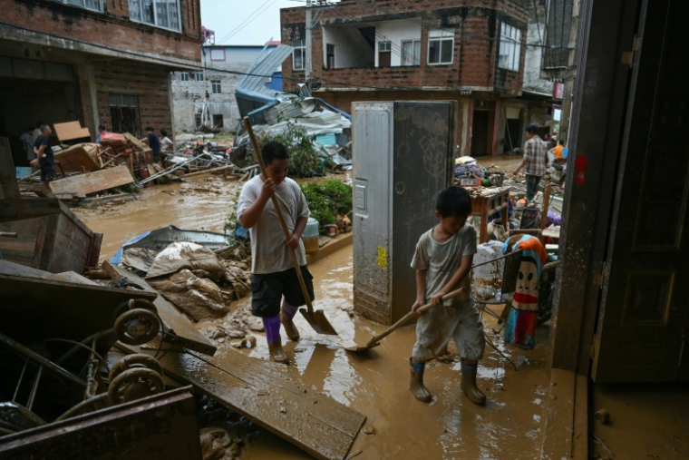 Des enfants aident à nettoyer la boue dans leur maison inondée lorsqu'un réservoir s’est effondré le 6 juillet, dans le village de Liulan, dans la ville de Hengzhou, dans la région du Guangxi, au sud-ouest de la Chine, le 8 juillet 2026 ( AFP / GREG BAKER )