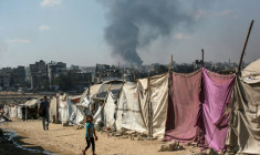 Des Palestiniens devant des tentes à Gaza-ville avec en arrière-plan une colonne de fumée s'élevant du centre de la bande de Gaza après un bombardement israélien, le 6 juillet 2025 ( AFP / Bashar TALEB )