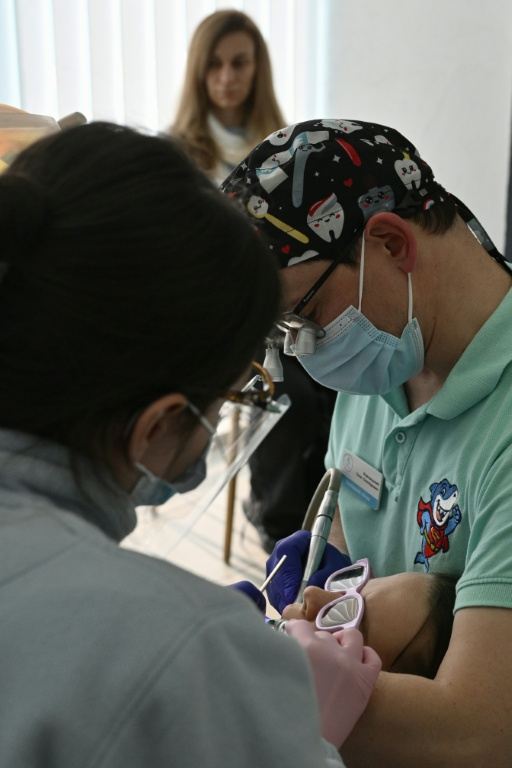 Le dentiste Oleg Kovnatskyï soigne une jeune patiente, Daryna Sidko, une réfugiée revenue en Ukraine pour soigner ses dents dans une clinique pour enfants à Kiev, le 30 avril 2026 ( AFP / Genya SAVILOV )