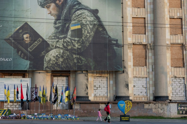 Une femme accompagnée d’un enfant passe devant le bâtiment endommagé de l’administration municipale et régionale de Kharkiv, le 20 octobre 2026 en Ukraine ( AFP / Tetiana DZHAFAROVA )