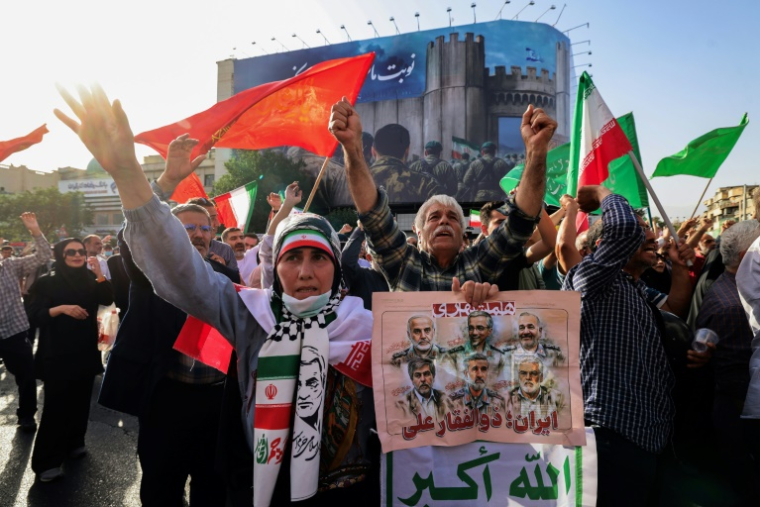 Des Iraniens brandissent des drapeaux et des pancartes lors d'un rassemblement de protestation contre l'attaque américaine en Iran sur la place Enghelab à Téhéran, le 22 juin 2025 ( AFP / ATTA KENARE )
