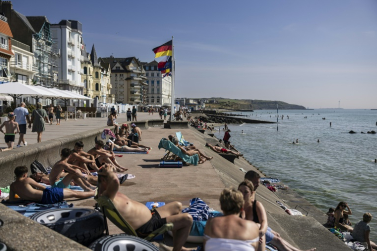 La plage de Wimereux le 18 juin 2025, avec ses baigneurs et sa gare voisine où s'abritent quelques migrants en quête d'ombre ( AFP / Sameer Al-DOUMY )