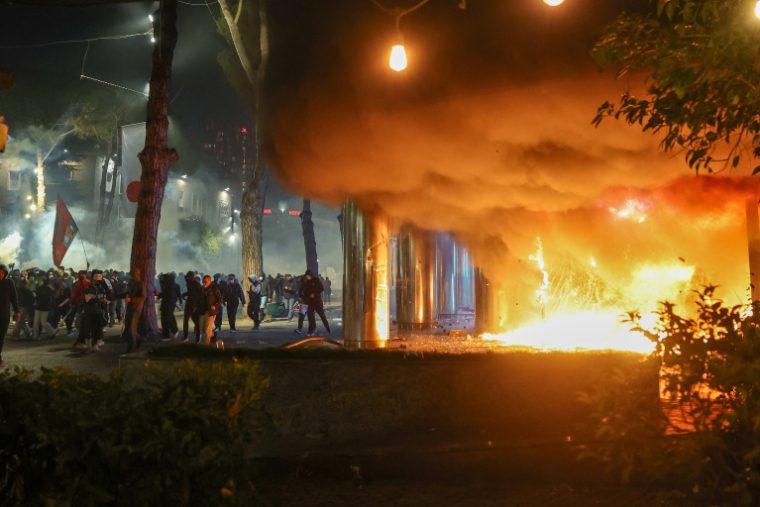 Des volutes de fumée s'échappent d'un incendie près d'un groupe de manifestants lors d'affrontements avec la police antiémeute dans le centre de Tirana, le 14 octobre 2026 ( AFP / Adnan Beci )