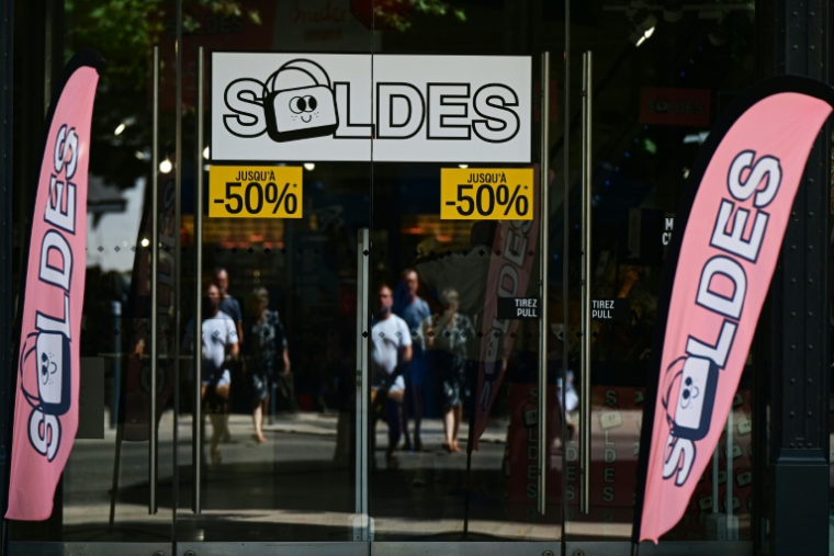 Des passants se tiennent devant la vitrine d'un magasin annonçant des réductions à l'occasion des soldes d'été, à Béziers, dans l'Hérault, le 28 juin 2025 ( AFP / GABRIEL BOUYS )