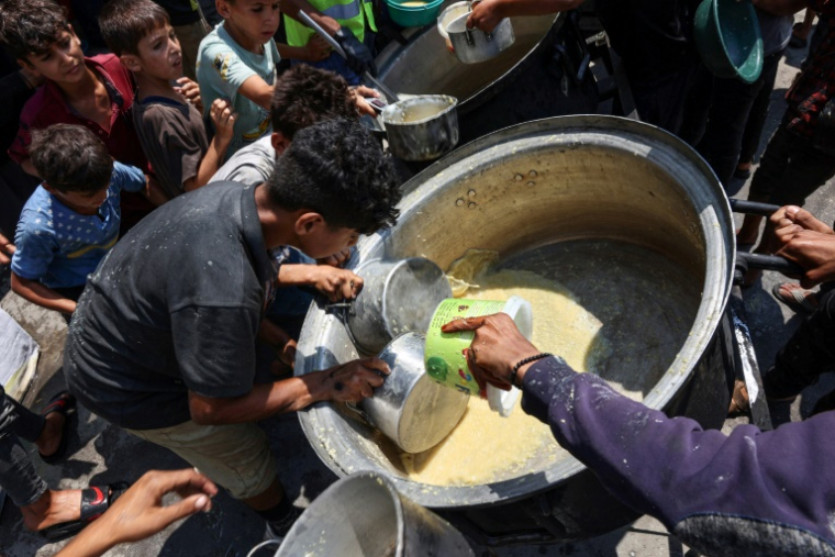 Des enfants palestiniens tentent de prendre ce qui reste dans un récipient de soupe aux lentilles dans un point de distribution de nourriture dans la ville de Gaza, le 25 juillet 2025 ( AFP / Omar AL-QATTAA )