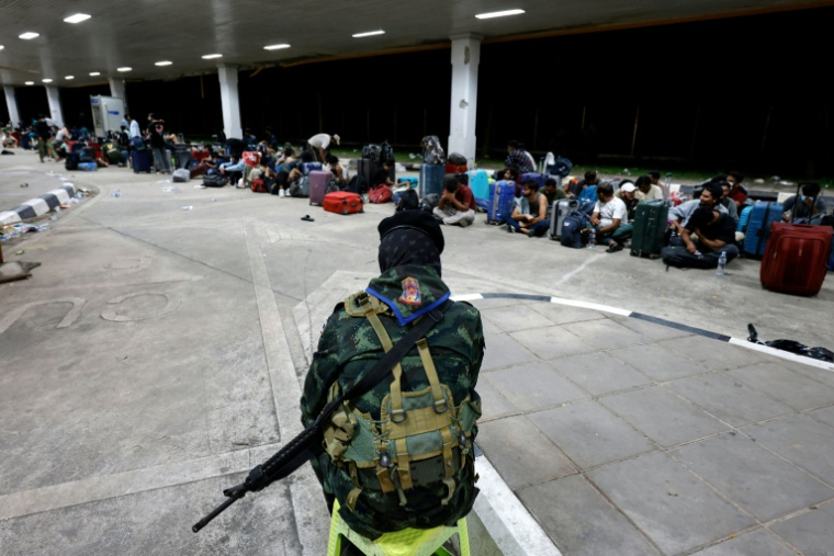 Un soldat thaïlandais surveille des personnes qui ont traversé la frontière depuis la Birmanie, en attente d'être contrôlées et interrogées par les autorités  dans le district de Mae Sot, dans la province de Tak, le 23 octobre 2025 ( THAI NEWS PIX / Sarot Meksophawannakul )