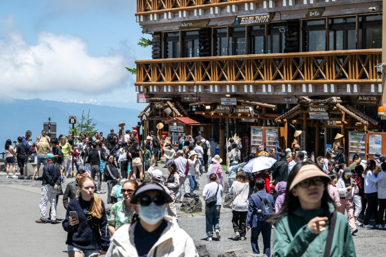 Des touristes devant le restaurant et la zone commerçante de la 5e station de la ligne Fuji Subaru. Cet endroit mène au sentier Yoshida populaire pour les randonneurs gravissant le mont Fuji, avant sa réouverture pour la saison à Narusawa (préfecture de Yamanashi), le 19 juin 2024. ( AFP / PHILIP FONG )