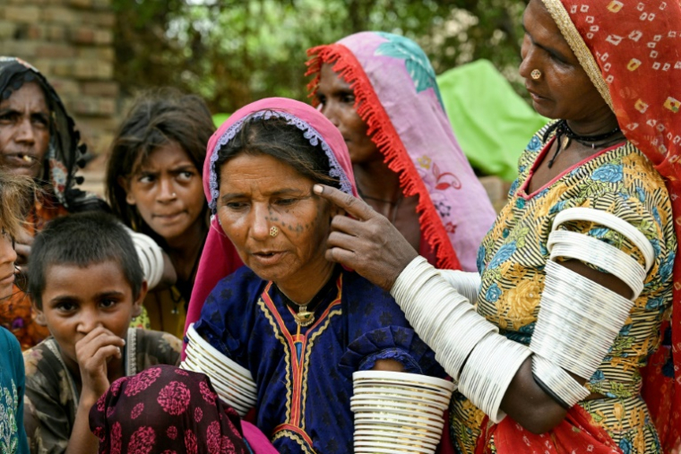 Une villageois en tenue traditionnelle montre un tatouage indigène encré sur le visage de Reshma (c) dans le village de Ponjo Kolhi, près d'Umerkot, un district à majorité hindoue, le 14 juillet 2025 au Pakistan ( AFP / Asif HASSAN )
