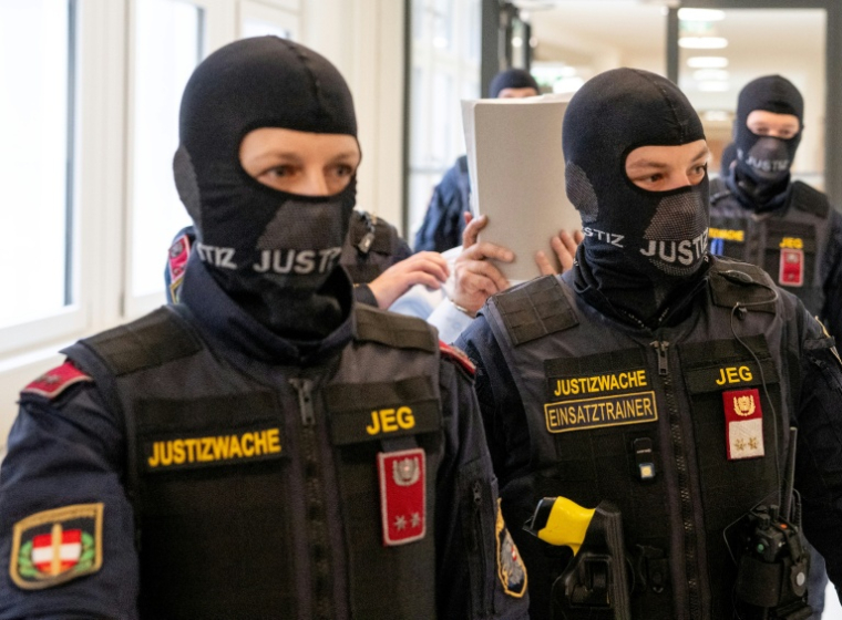 L'ancien général syrien et accusé Khaled al-Halabi (c) cache son visage alors qu'il est escorté par des agents de justice pour son procès au tribunal régional de Vienne, le 1er juin 2026 en Autriche ( AFP / Joe Klamar )