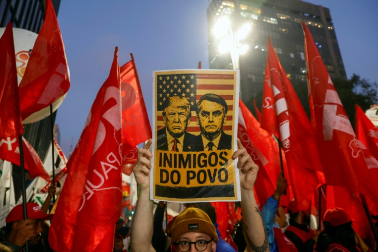 Un homme tient une pancarte avec des images du président américain Donald Trump et de l'ancien président brésilien Jair Bolsonaro sur laquelle on peut lire « Ennemis du peuple » lors d'une manifestation à Sao Paulo, au Brésil, le 10 juillet 2025 ( AFP / Miguel SCHINCARIOL )