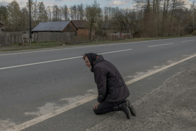 Une femme agenouillée sur le bord de la route en attendant le passage d'un bus de prisonniers de guerre ukrainiens libérés par la Russie, dans un lieu non dévoilé de la région de Tcherniguiv, le 24 avril 2026  ( AFP / Roman PILIPEY )