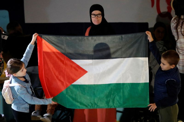 Une femme regarde des enfants tenant un drapeau palestinien