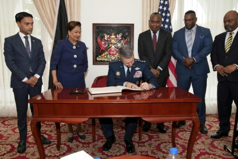 Photo diffusée par le bureau de presse de la présidence de Trinité-et-Tobago montrant le chef d'état-major américain, le général Dan Cain (c)e, signant un document avec la Première ministre de Trinité-et-Tobago, Kamla Persad-Bissessar (2e g), lors de sa visite à Port of Spain, le 25 novembre 2025 ( Présidence de Trinité-et-Tobago / Handout )