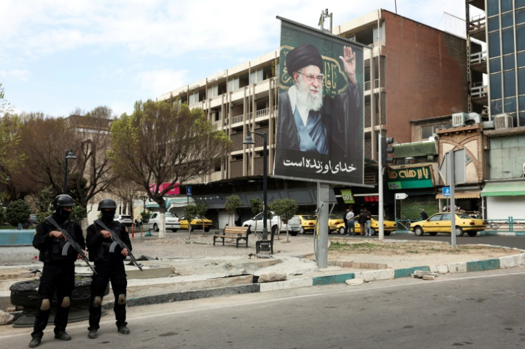 Des membres des forces de sécurité iraniennes montent la garde dans une rue de Téhéran, près d'un panneau d'affichage à l'effigie du guide suprême iranien, l'ayatollah Ali Khamenei, le 2 mars 2026 ( AFP / - )