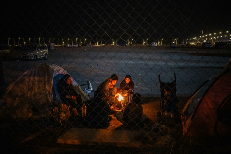 Une famille de déplacés se réchauffe devant une tente sur le front de mer de Beyrouth le 18 mars 2026 ( AFP / DIMITAR DILKOFF )