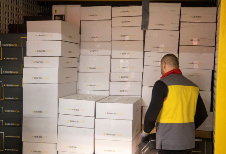 Un livreur se tient à côté de colis Zalando dans un centre de tri suisse