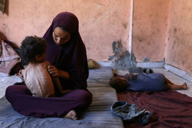 Une Palestinienne est assise avec son fils mal nourri de 2 ans, Yazan, dans leur maison endommagée du camp de réfugiés d'Al-Chati, dans la ville de Gaza, le 23 juillet 2025 ( AFP / Omar AL-QATTAA )