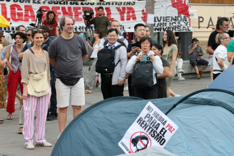 Des touristes prennent des photos des tentes dressées par des manifestants qui protestent contre les expulsions et la crise du logement, le 27 septembre 2026 à Madrid ( AFP / Thomas COEX )