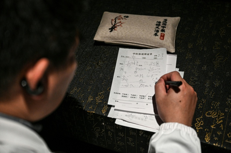 Le Dr Ding, praticien de médecine traditionnelle chinoise, rédige une ordonnance dans un bar à cocktails à Shanghai, le 3 février 2026 en Chine ( AFP / Jade GAO )