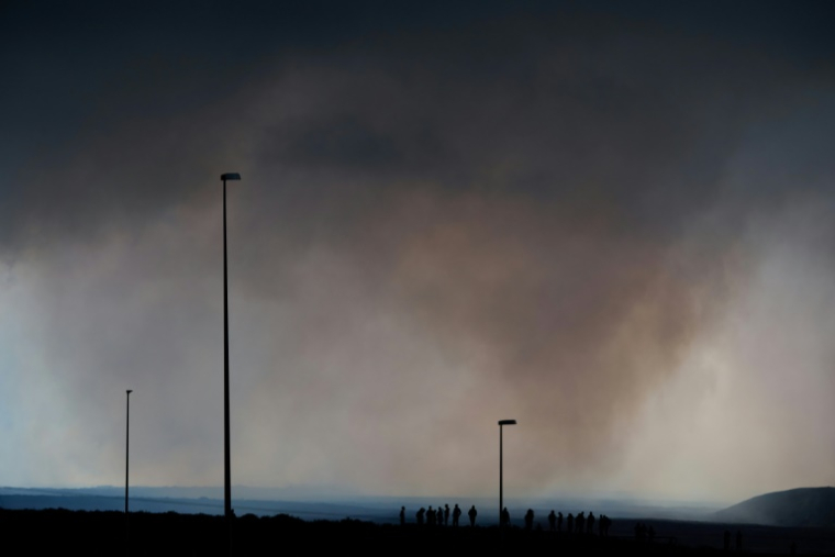 Des touristes sur une route près de l'aéroport de Keflavik, en Islande, le 16 juillet 2025, observent des nuages de fumée au loin émanant d'un volcan près de Grindavik sur la péninsule islandaise de Reykjanes, après son éruption ( AFP / Halldor KOLBEINS )
