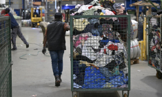 Un employé tire un chariot rempli de vêtements de seconde main destinés au tri au centre de recyclage « Le Relais » à Acigné, près de Rennes, Le 21 juillet 2025. ( AFP / DAMIEN MEYER )