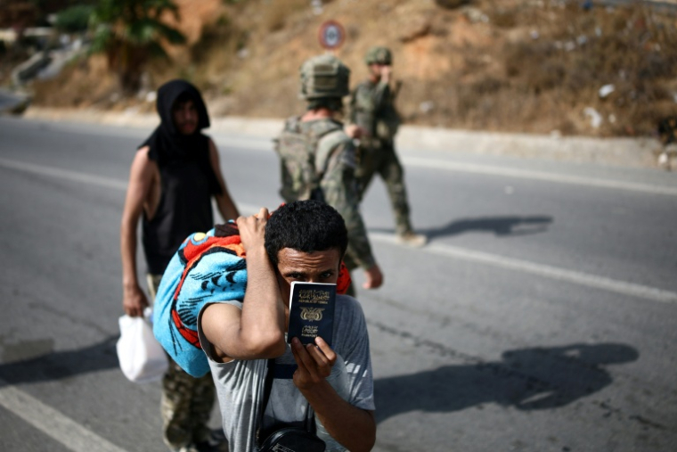 Un candidat à l'émigration montre son passeport yéménite alors qu'il est raccompagné par des militaires jusqu'au poste-frontière entre le Maroc et l'enclave espagnole de Ceuta, le 2 août 2026  ( AFP / Henry Nicholls )