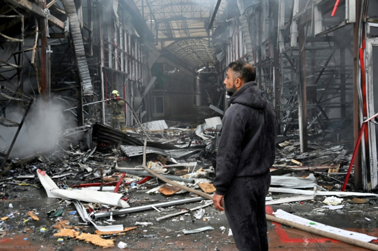 Un homme observe les dégâts alors qu'un pompier ukrainien éteint un incendie au marché "Barabashovo" après une attaque de drone à Kharkiv, le 6 mai 2025 en Ukraine ( AFP / SERGEY BOBOK )