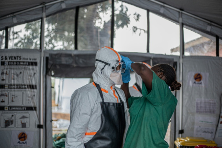 Une soignante aide un médecin à mettre son équipement de protection individuelle (EPI) avant d'entrer dans le centre de traitement Ebola (CTE) de Rwampara pour soigner des patients atteints de la maladie à virus Ebola, le 13 juillet 2026 à Bunia, dans la province de l'Ituri, en RDC ( AFP / BENEDICTION MURHABAZI )
