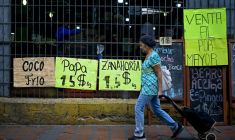 Une femme tire un chariot de courses à roulettes devant un supermarché qui affiche sur des panneaux les prix des aliments en dollars américains à Caracas, le 22 avril 2026 ( AFP / Federico PARRA )