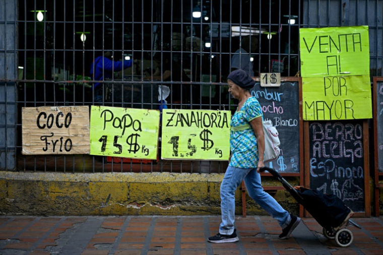 Une femme tire un chariot de courses à roulettes devant un supermarché qui affiche sur des panneaux les prix des aliments en dollars américains à Caracas, le 22 avril 2026 ( AFP / Federico PARRA )