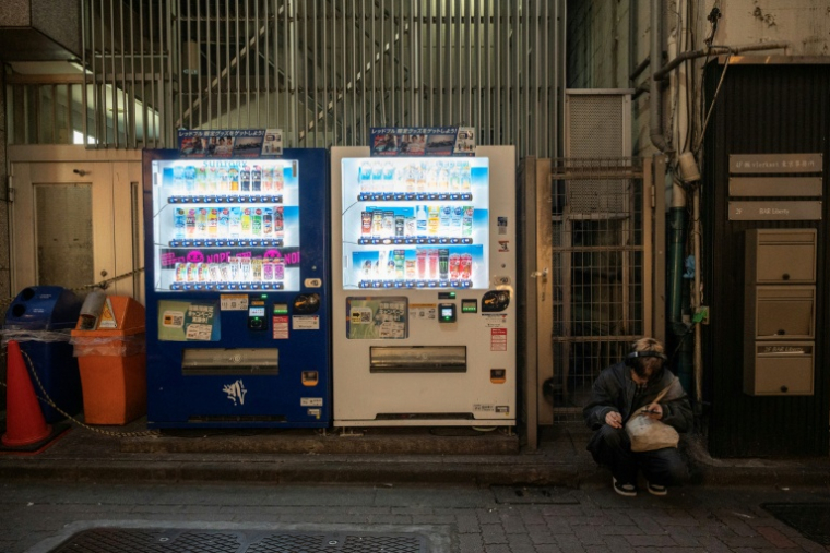 Un homme assis à côté de distributeurs automatiques, le 13 avril 2026 à Tokyo ( AFP / Andrew CABALLERO-REYNOLDS )