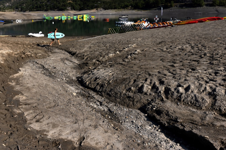 Le lac de Serre-Ponçon, dans les Alpes, à une cinquantaine de kilomètres de la station du Grand Puy, le 25 août 2022. This view taken on August 25, 2022, shows a man carrying a water ski-ing board on the Serre-Ponçon lake at Ubaye Serre-Ponçon in The French Alps, as water levels decreased 16 meters due to the drought. The latest monthly analysis by the European Union's Global Drought Observatory (GDO) highlighted the risk of ongoing soil dryness caused by successive heatwaves and a persistent lack of rainfall as it maintained its warning issued with the previous report that nearly half of the EU's territory is at risk of drought. (Photo by JOEL SAGET / AFP) ( AFP / JOEL SAGET )