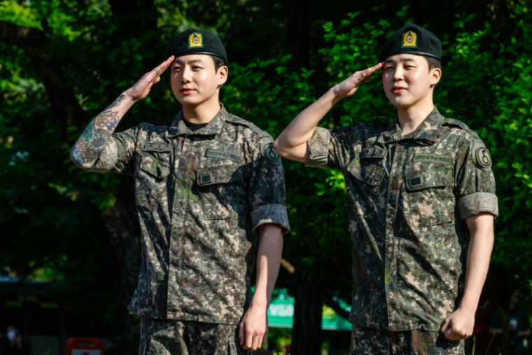 Deux des membres du boys band de K-pop BTS, Jungkook (g) et Jimin font le salut militaier à leur arrivée à Yeoncheon, le 11 juin 2025 en Corée du Sud, peu après leur libération de 18 mois de service militaire ( AFP / ANTHONY WALLACE )