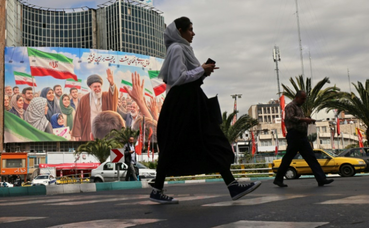 Une femme marche devant un immense panneau d’affichage représentant le guide suprême iranien tué, l’ayatollah Ali Khamenei, sur la place Valiasr à Téhéran, le 19 avril 2026 ( AFP / ATTA KENARE )