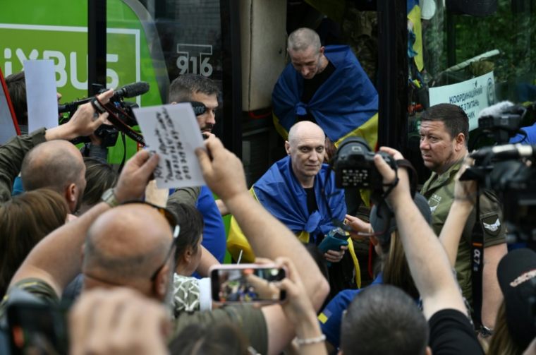 Des prisonniers de guerre ukrainiens libérés enveloppés dans le drapeau national débarquent d'un bus à leur arrivée après un échange de prisonniers dans la région de Tcherniguiv, le 26 juin 2025, en Ukraine ( AFP / Genya SAVILOV )
