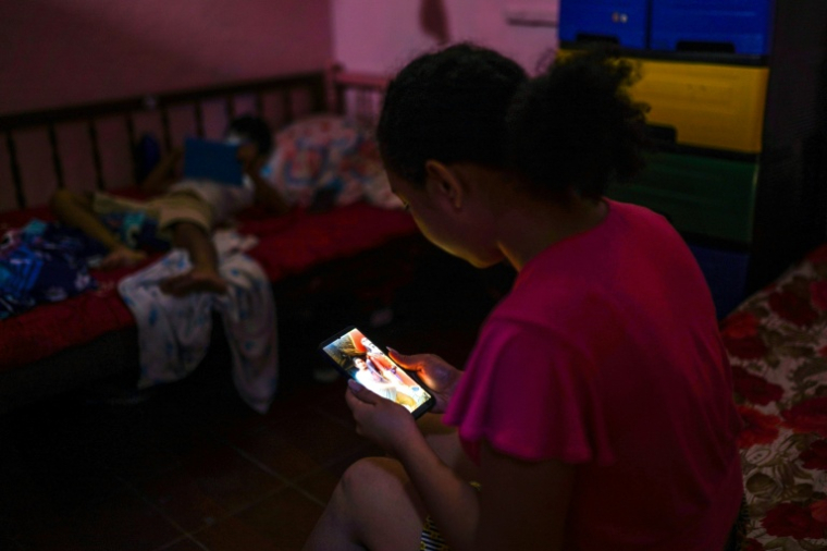 Carmen, 17 ans, regarde une photo de son père sur son téléphone, le 12 décembre 2025 à Zacatecoluca, au Salvador ( AFP / STRINGER )