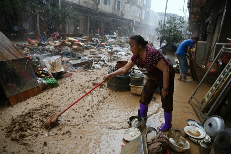 Une habitante repousse la boue dans une zone inondée après la rupture d'un réservoir près de Gantang, dans la région du Guangxi, le 9 juillet 2026 dans le sud-ouest de la Chine ( AFP / GREG BAKER )