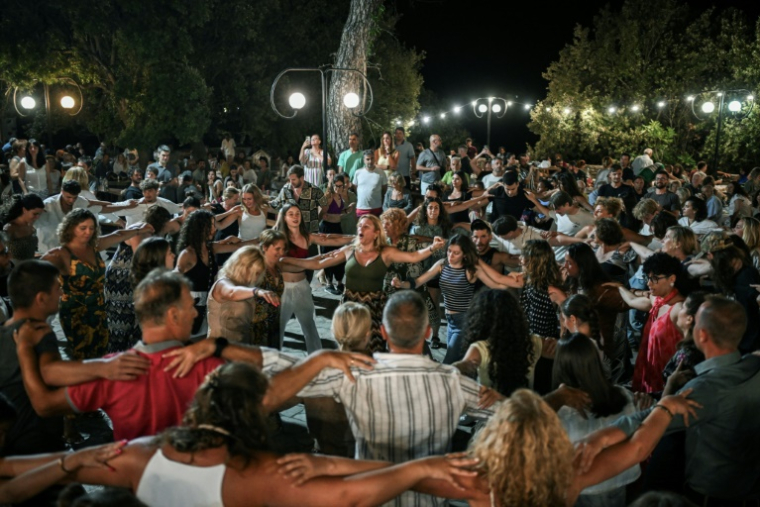 Locaux et vacanciers dansent un "panigiri", une tradition en Grèce, au village du Prophète Elie, sur l'île d'Ikaria, le 20 juillet 2025 "panigiri" in the village of Profitis Ilias on the Greek Aegean island of Ikaria, on July 20, 2025. The "panigiri" are patron saint festivals that mark the summer in all the villages of the Greek islands and on the mainland, deeply rooted in Greek culture. Celebrations and dances often continue until dawn, attracting large crowds and many tourists. Each "panigiri" is associated with the feast day of a local patron saint, such as the Prophet Elijah on July 20 and Saint John on August 28. Its origins date back to 1821. ( AFP / Aris MESSINIS )