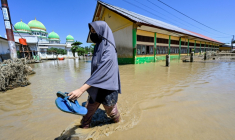 Une habitante marche près d'une mosquée dans zone inondée, le 30 novembre 2025 à Meureudu en Indonésie ( AFP / CHAIDEER MAHYUDDIN )