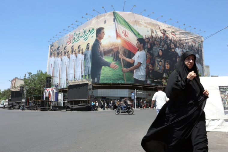 Une Iranienne passe devant un panneau d'affichage géant mettant en scène l'équipe nationale iranienne de football qui a pris la direction de la Turquie pour y préparer le Mondial-2026, le 18 mai 2026 à Téhéran ( AFP / - )