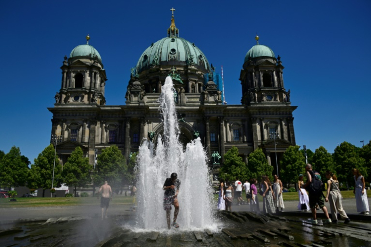 Des personnes se rafraîchissent dans l'eau d'une fontaine, le 2 juillet 2025 à Berlin ( AFP / John MACDOUGALL )